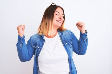 İzole edilmiş beyaz arka plan üzerinde duran kot gömlekli güzel bir kadın kolları havada ve gözleri kapalı bir şekilde başarıyı kutluyor ve hayrete düşüyor. Kazanan konsept.