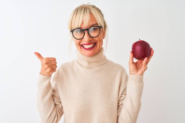 Elma tutan orta yaşlı bir kadın izole edilmiş beyaz arka planda duruyor. Kocaman gülümsüyor. Tamam işareti yapıyor.