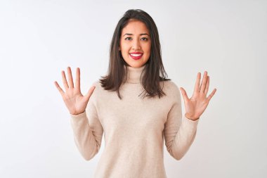 Balıkçı yaka kazak giyen güzel Çinli kadın izole edilmiş beyaz arka plan üzerinde duruyor ve parmaklarıyla on numarayı gösterirken kendinden emin ve mutlu gülümsüyor..