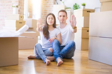 Genç ve güzel bir çift, yeni evlerinde karton kutuların etrafında oturmuş ellerinde dur işareti, ciddi ve kendinden emin bir ifadeyle savunma jesti yapıyorlar.