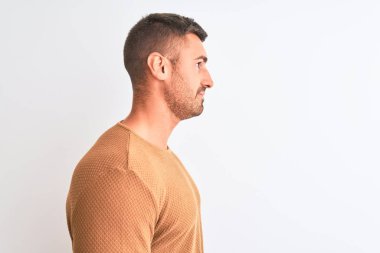 Kışlık süveter giyen yakışıklı genç bir adam yalıtılmış arka plana bakıyor, rahat bir görünüm takınıyor kendine güvenen bir gülümsemeyle doğal bir yüz ifadesi sergiliyor..