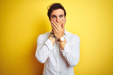 Zarif tişört giyen yakışıklı genç işadamı, izole edilmiş sarı arka planda dikiliyor. Ağzını yanlışlıkla ellerle kapatıyor. Gizli konsept.
