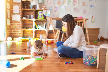 Anaokulundaki bir sürü oyuncağın etrafında dijital tahta kullanarak güzel öğretmen ve bebek çizimi yapıyorlar.