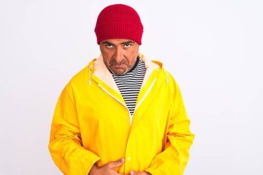 İzole edilmiş beyaz arka planda duran yağmurluk ve yün şapka giyen orta yaşlı bir adam depresif ve endişeli, sinirli ve korkmuş bir halde duruyor. Üzücü ifade.