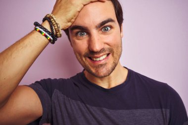 İzole edilmiş pembe arka planda dikilen sıradan tişört giyen genç yakışıklı adam elleri başının üstünde, utanç ve şaşkınlık dolu, sinirli ve hayal kırıklığına uğramış bir halde. Hata için korku ve üzüntü.