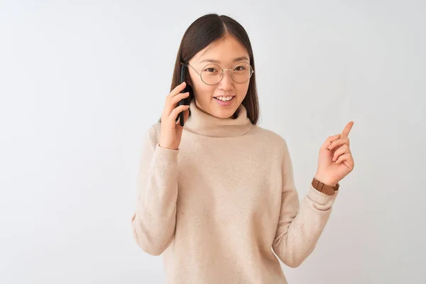 年轻的中国女人在智能手机上通过孤独的白色背景愉快地交谈 满脸笑容 手指手画脚地朝旁边走去 脸上带着快乐而自然的表情 — 图库照片