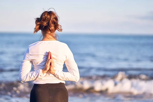 Young beautiful sportwoman practicing yoga. Coach standing on bakcview teaching reverse prayer pose at the beach