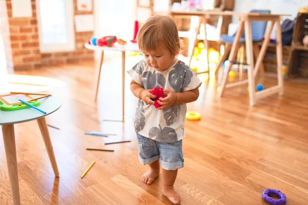 愛らしい幼児は幼稚園でおもちゃの多くの周りにブロックを構築して遊んでいます — ストック写真