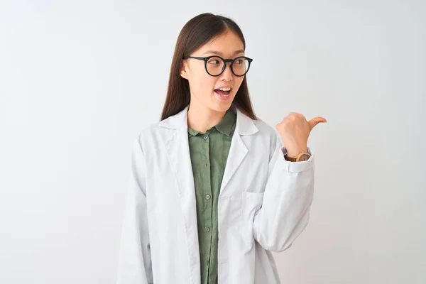 若いです中国の科学者女性身に着けていますコートと眼鏡上の隔離された白い背景笑顔で幸せな顔見ますと指で側面を指していますアップ — ストック写真