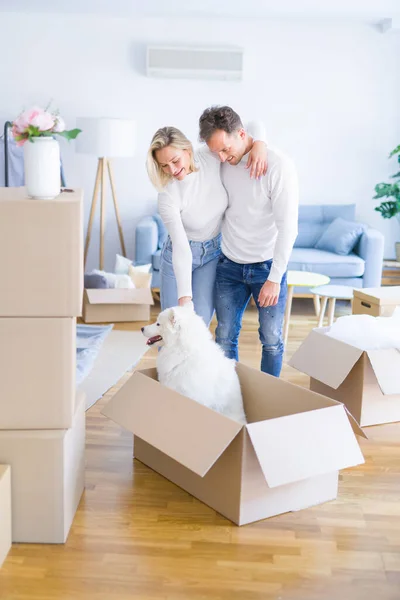 Young beautiful couple with dog hugging at new home around cardboard boxes