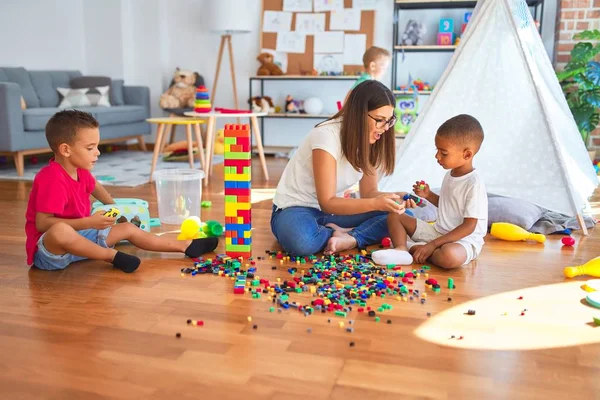 幼稚园里 年轻漂亮的老师和幼儿在许多玩具周围玩积木游戏 — 图库照片