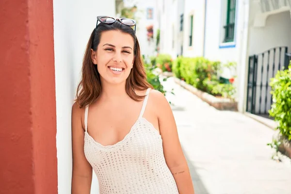 Young beautiful woman at the colorful village of Puerto de Mogan, smiling happy at the street leaning on white wall on summer holidays