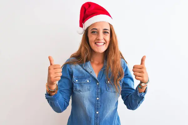 孤立した背景の成功の印の上にクリスマスの帽子を身に着けている若い美しい赤毛の女性は手で肯定的なジェスチャーをし 親指を笑顔と幸せ 陽気な表情と勝者のジェスチャー — ストック写真