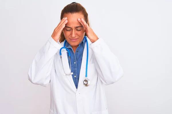 ストレスが原因で頭の痛みのために頭の上に手で孤立した背景に聴診器を身に着けている中年の成熟した医師の女性 片頭痛に苦しむ — ストック写真