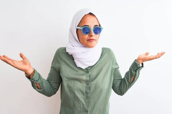 孤立した背景にヒジャーブと夏のサングラスをかけている若いアラブ人女性は 腕や手で上げられた混乱した表情をしています 疑いの概念 — ストック写真
