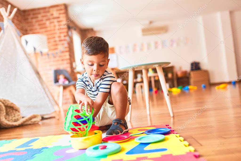 Beautiful toddler boy sitting on puzzle playing meals with plastic plates, fruits and vegetables at kindergarten