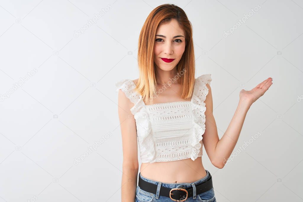 Beautiful redhead woman wearing casual t-shirt standing over isolated white background smiling cheerful presenting and pointing with palm of hand looking at the camera.