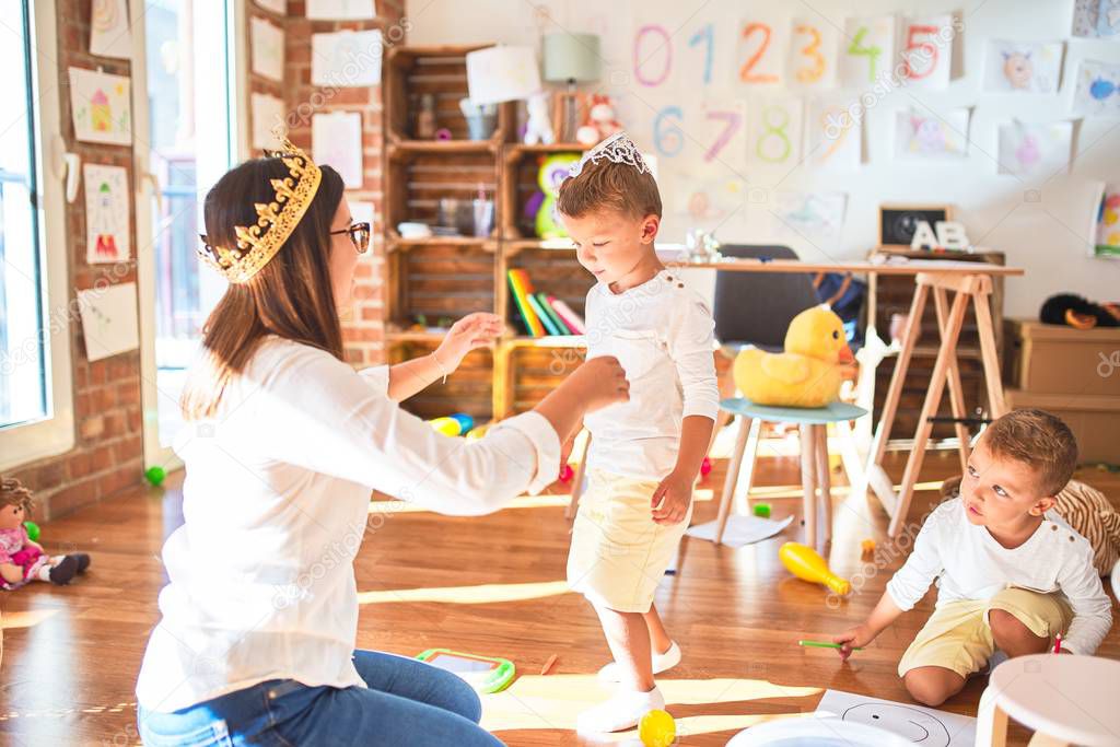 Beautiful teacher and toddlers playing with king crown around lots of toys at kindergarten