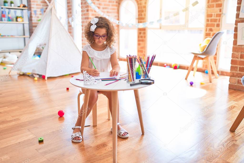 Beautiful toddler wearing glasses sitting drawing using paper and pencils at kindergarten