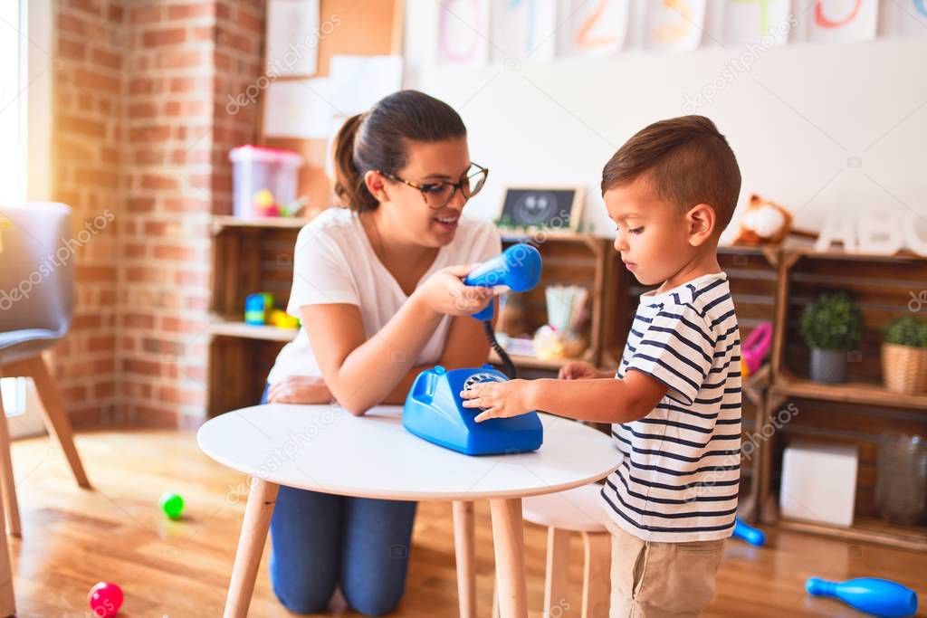 Beautiful teacher and toddler boy playing with vintage blue phone at kindergarten