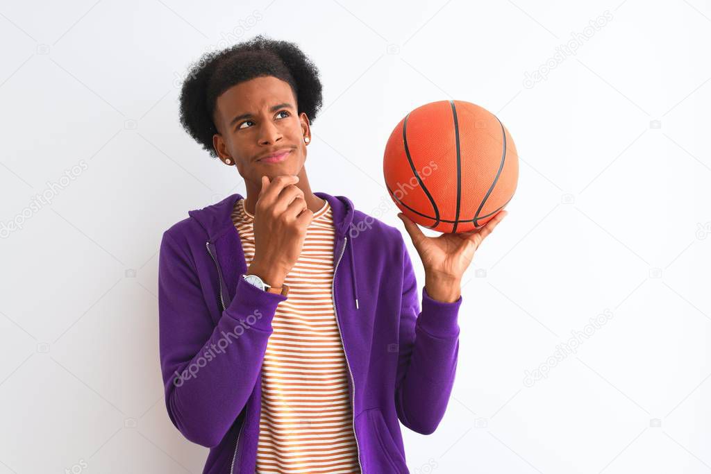 Young african american sportsman holding basketball ball over isolated white background serious face thinking about question, very confused idea