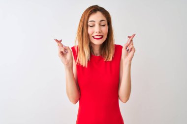 Kırmızılı iş kadını zarif kırmızı elbiseler giyiyor. İzole edilmiş beyaz arka plan üzerinde duruyor. Umut ve gözler kapalı gülümseyerek el işareti yapıyor. Şans ve batıl inanç..