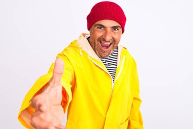 Yağmurluk ve yünlü şapka giyen orta yaşlı bir adam izole edilmiş beyaz arka planda durup dostça gülümseyerek selamlama ve hoş geldin diyor. Başarılı bir iş..