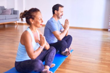 Orta yaşlı, güzel, sportif bir çift mindere oturmuş yoga yapıyor, spor salonunda dua ediyor.