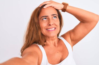 Orta yaşlı olgun bir kadın, izole edilmiş arka plan üzerinde akıllı telefon kullanarak fotoğraf çekiyor. Elleri başının üstünde, utanç ve şaşkınlık dolu, sinirli ve hayal kırıklığına uğramış bir şekilde. Hata için korku ve üzüntü.