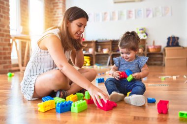 Genç, güzel öğretmen ve bebek anaokulunda yapı taşı oyuncaklarıyla oynuyorlar.