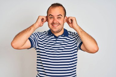 Sıradan çizgili polo giyen genç adam izole edilmiş beyaz arka planda duruyor parmaklarıyla kulaklarını çekerek gülümsüyor, komik bir jest. Seçme sorunu