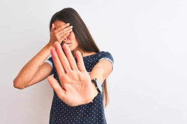 Mavi günlük tişört giyen genç ve güzel bir kadın izole edilmiş beyaz arka plan üzerinde duruyor gözleri ellerle kapıyor ve üzgün ve korku ifadeleriyle jest yapıyor. Utanç verici ve olumsuz bir kavram..