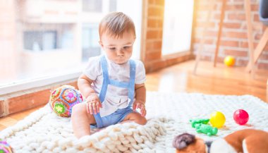Anaokulunda battaniyenin üzerinde bir sürü oyuncağın etrafında oturan güzel çocuk.