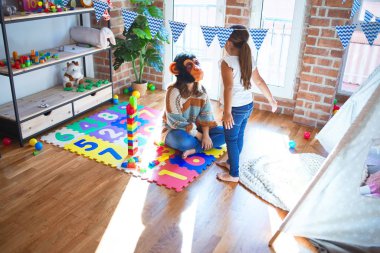 Anaokulunda bir sürü oyuncağın etrafında maymun maskesiyle oynayan güzel öğretmen ve bebek.
