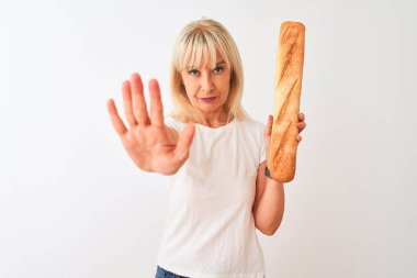 Orta yaşlı fırıncı kadın izole edilmiş beyaz arka planı üzerinde duran, elinde dur işareti olan, ciddi ve kendinden emin bir ifadeyle savunma hareketi yapan bir ekmek tutuyor.
