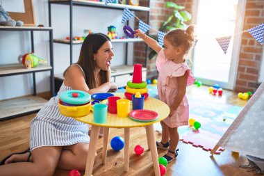 Genç, güzel öğretmen ve bebek, anaokulundaki masada halkalar kullanarak piramit inşa ediyorlar.