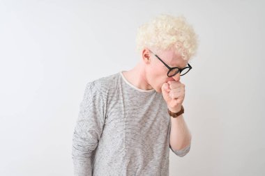 İzole edilmiş beyaz arka plan üzerine çizgili tişört ve gözlük takan genç, sarışın adam kendini kötü hissediyor ve soğuk algınlığı veya bronşitin belirtisi olarak öksürüyor. Sağlık hizmetleri kavramı.