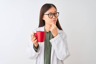 Genç Çinli kadın gözlük takıyor. İzole edilmiş beyaz arka planda kahve içiyor. Ciddi bir yüz.