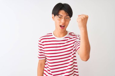 Gözlüklü ve çizgili tişörtlü genç Çinli adam izole edilmiş beyaz arka planda kızgın ve kızgın duruyor öfkeyle bağırırken yumruğunu kaldırıyor. Öfke ve agresif kavram.