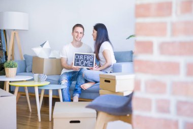 Karton kutular etrafında yeni evde mesaj ile kara tahta tutan kanepede oturan genç güzel çift