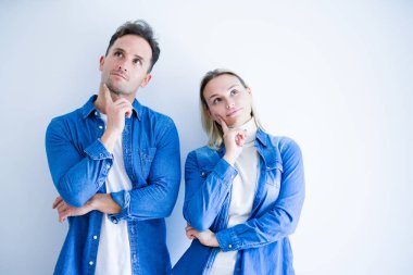 Young beautiful couple wearing denim shirt standing over isolated white background with hand on chin thinking about question, pensive expression. Smiling with thoughtful face. Doubt concept. clipart
