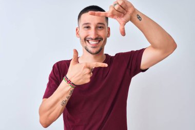 İzole edilmiş arka planda duran yakışıklı genç adam gülümsüyor ve elleri ve parmakları gülen yüzlü bir çerçeve yapıyor. Yaratıcılık ve fotoğrafçılık kavramı.