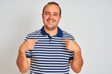 İzole edilmiş beyaz arka planda duran sıradan çizgili polo giyen genç adam yüzünde bir gülümsemeyle gururlu ve mutlu bir şekilde kendini işaret ediyor..