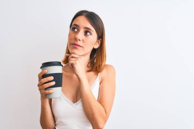 Güzel kızıl saçlı kadın, izole edilmiş arka planda kahve içerken ciddi bir yüz düşünüyor, kafası karışmış bir fikir.