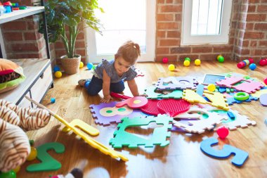 Anaokulunda yerde oturmuş oyuncaklarla oynayan güzel bir çocuk.