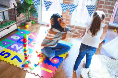 Anaokulunda bir sürü oyuncağın etrafında maymun maskesiyle oynayan güzel öğretmen ve bebek.