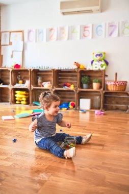 Anaokulunda elinde bir kavanoz çikolata renkli topla yerde oturan güzel çocuk.