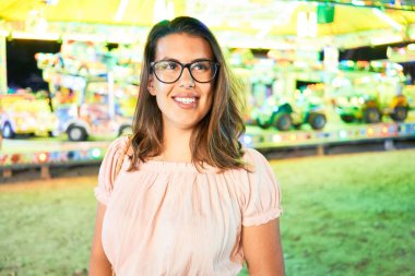 Gözlük takan genç ve güzel bir kadın gecenin ışıklarında mutlu ve heyecanlı bir şekilde gülümsüyor.