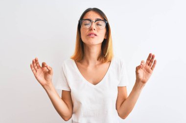 Gözlüklü kızıl saçlı güzel bir kadın izole edilmiş arka planda rahatla ve gözleri kapalı gülümse parmaklarıyla meditasyon hareketi yapıyor. Yoga konsepti.