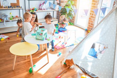 Güzel öğretmen ve bir grup çocuk anaokulunda bir sürü oyuncakla oynuyorlar.